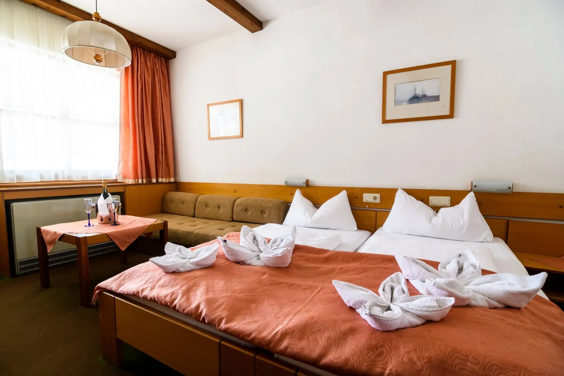 A hotel egyik szobája két külön ággyal, terrakotta színű ágyterítővel és kanapéval